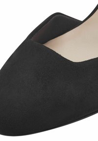 Chaussure plate en suede noir avec un bout pointu et des côtés ouverts. Doublure intérieure lisse et extérieur texturé créent une finition mate.