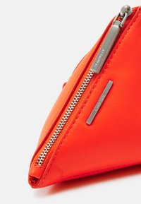 Neceser triangular de cuero naranja con cremallera y herrajes plateados. Presenta una textura suave y un acento de logo metálico.