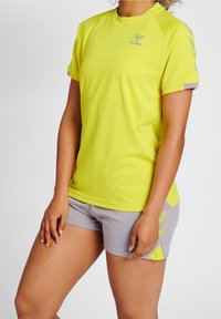 Gul sport t-shirt med kort ärm, med en grå accent på ärmarna. Para med grå shorts som har ett diagonalt randigt mönster.