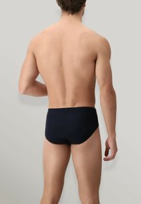 Slip da bagno blu navy, realizzati in tessuto elastico, presentano una vestibilità aderente e un design aerodinamico, mettendo in mostra una texture liscia e una copertura minima.