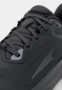 Scarpa da corsa nera con tomaia in mesh testurizzato, occhielli rinforzati, lacci piatti e design elegante. Accento del logo distintivo sul lato.