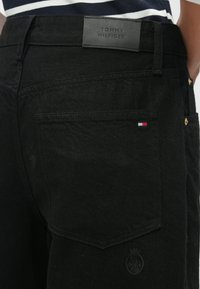 Čierne džínsy s koženou nášivkou na páse, s jemným prešívaním a malou trojfarebnou vlajkou pri zadnej vrecku.