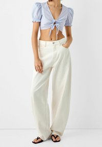 Svetle modrá zkrácená blůza s nabíranými rukávy a vázáním vpředu, spárovaná s volnými bílými džíny s vysokým pasem.