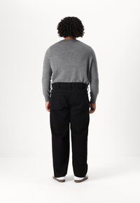Pulover gri cu mâneci lungi, pantaloni negri și adidași albi. Puloverul are un decolteu rotund; pantalonii au un croi clasic și buzunare.