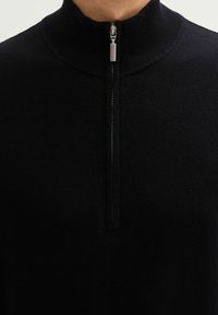 Czarny pulower z kieszenią na zamek błyskawiczny, z prążkowanym kołnierzem i gładką fakturą. Posiada srebrny zamek oraz minimalistyczny design bez wzorów czy ozdób.