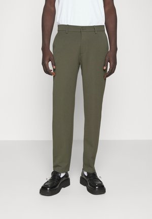 Olive green tailored pants with a flat front, belt loops, and a button closure. Worn with black loafers and white socks.