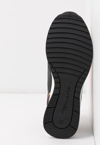 Semelle en caoutchouc noir d'une chaussure avec des rainures horizontales, nom de marque "Tamaris" et numéro de taille 37 visible sur la semelle.