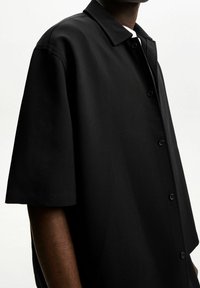 Czarna koszula na krótki rękaw z gładkiej tkaniny. Posiada klasyczny kołnierzyk oraz pięć guzików z przodu. Prosty wzór.