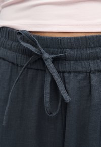 Κοντινό πλάνο ενός δεμένου σκουρόχρωμου γκρι κορδονιού σε ελαστική μέση φαρδιών παντελονιών με ανοιχτό ροζ επάνω χείλος ορατό επάνω.