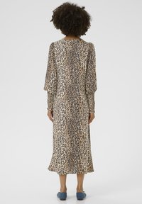 Leopard print dress with long puff sleeves, a relaxed silhouette, and smocked cuffs. Made from lightweight fabric in beige and brown tones.