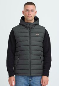 Tumehall puffer vest, millel on kapuuts, joonistatud mustri ja lukuga, külgtaskud. Ühildatud musta pika varrukaga särgiga all.