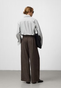 Camicia a righe grigio chiaro con bottoni, pantaloni larghi marroni e borsa nera. Gli accessori includono occhiali da sole neri e orecchini a cerchio.