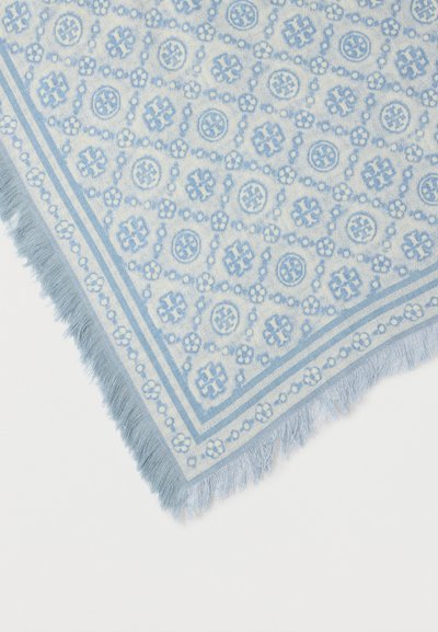 Coin de tissu à motifs bleu clair et blanc avec des dessins géométriques et floraux et des bords à franges sur un fond blanc.