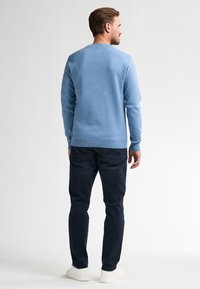 Lichtblauwe gebreide trui met lange mouwen, ronde halslijn en geribde zoom, gecombineerd met donkerblauwe broek en witte sneakers.