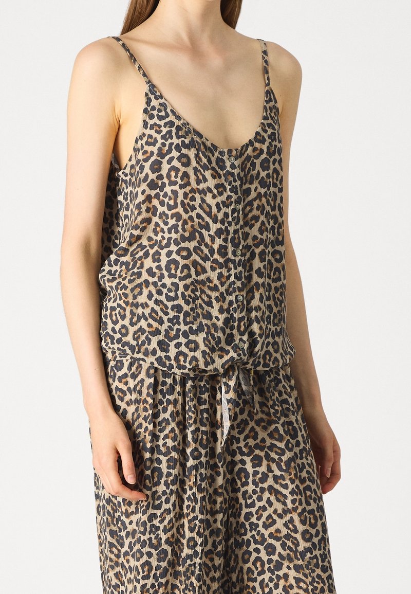 Femme portant une robe sans manches à imprimé léopard avec des boutons sur le devant et une ceinture nouée à la taille.