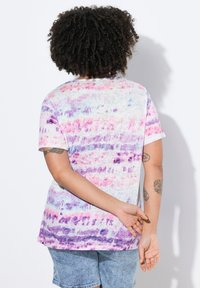 T-shirt med korte ærmer i lys grå med et tie-dye mønster i pink og lilla. Blød tekstur, afslappet pasform, med en buet kant.