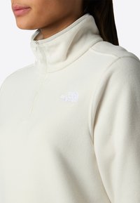 Witte fleece pullover met een ritskraag, voorzien van een klein reliëflogo op de borst en een textuurstof voor warmte.