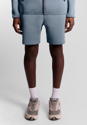 Lichtblauwe sportshorts van zachte stof, met een eenvoudig ontwerp. Gecombineerd met grijze en beige sneakers en witte crew-sokken.