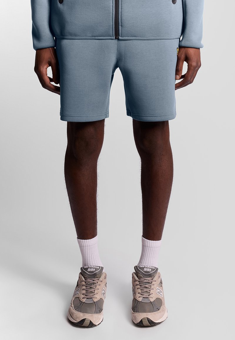 Pantaloni sportivi azzurri chiari realizzati in tessuto morbido, con un design semplice. Abbinati a sneakers grigie e beige e calzini bianchi alla caviglia.