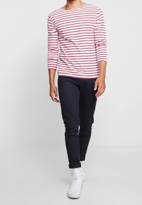 Czerwona i biała koszula w paski z długim rękawem zestawiona z ciemnoniebieskimi, slim fit spodniami i białymi trampkami, z podwiniętymi mankietami i luźnym krojem.