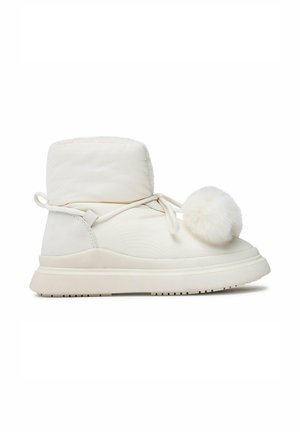 Winterlicher knöchelhoher Stiefel in Cremefarbe mit dicker Sohle, Schnürung vorne, die zu einer Schleife gebunden ist, und einer großen flauschigen Bommel-Dekoration an der Seite.
