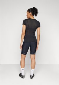 Svart atletisk skjorte med korte ermer og mesh rygg, kombinert med sykkelshorts med midjebånd i en slank design; hvite og grå detaljer på sokkene.