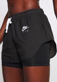Los pantalones cortos Nike Air negros presentan una tela ligera y transpirable con una cinturilla elástica y cuerdas blancas, mostrando un logo en la parte frontal.