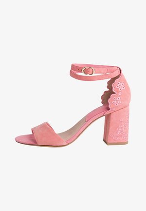 Růžová semišová sandála na vysokém podpatku s páskem kolem kotníku, otevřenou špičkou a blokovým podpatkem, zdobená květinovou výšivkou a vroubkovanými okraji.