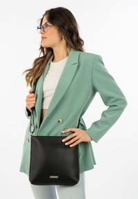 Black leather crossbody bag with a textured finish, featuring a gold hardware accent and a simple design. Worn by a model in a mint green blazer.