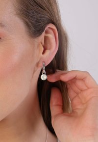 Boucles d'oreilles en argent sterling avec un pendentif en pierre opaque de forme circulaire. Elles présentent une finition polie et un fermoir à levier, mettant en avant un design minimaliste.