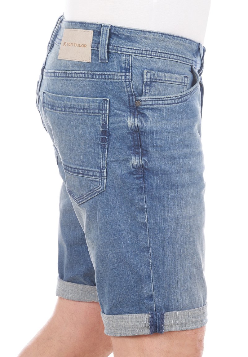 Shorts de mezclilla en azul medio con una textura ligeramente desgastada, dobladillo enrollado y detalle en el bolsillo trasero con un parche de cuero marrón.