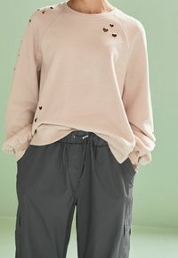 Felpa rosa chiaro con tagli a forma di cuore sulle spalle, abbinata a pantaloni cargo grigio scuro con vita elasticizzata e tasche laterali.