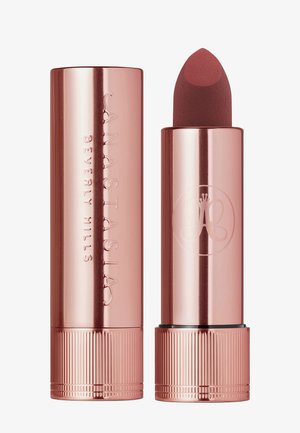 Rose gold lipstick tube with a rounded tip. Etched brand name and logo on the surface. Matte lipstick visible, displayed upright.