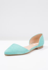 Turkos mocka platt sko med spetsig tå, öppen häl-design och en låg träklack. Mjuk textur och minimalistisk stil.