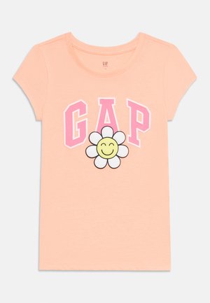 Hellpfirsichfarbenes Kinder-T-Shirt mit kurzen Ärmeln, pinkem "GAP"-Schriftzug und einem lächelnden weißen Gänseblümchen in der Mitte.