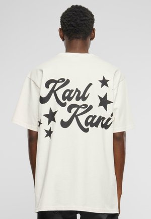 Balta per didelį dydį t-shirt, su didelėmis juodomis raidėmis „Karl Kani“ ir juodomis žvaigždžių grafikomis ant nugaros. Trumpomis rankovėmis, pagaminta iš medvilnės.