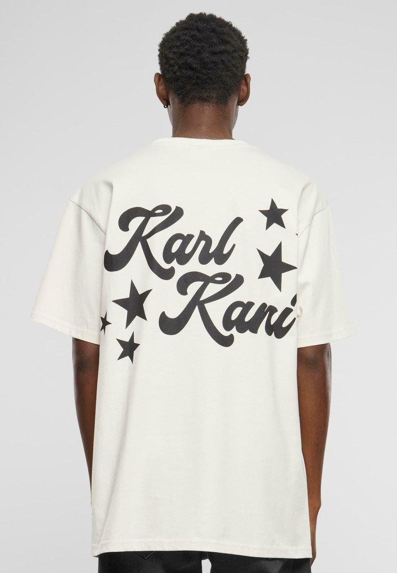 Hvit oversized t-skjorte med stor svart tekst som leser "Karl Kani" og svarte stjernemotiver på baksiden. Korte ermer, laget av bomull.