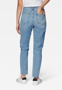 Vaqueros de mezclilla azul claro con corte recto, cinco bolsillos, costuras visibles y un leve desgaste. Combinados con zapatillas blancas y negras.