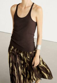 Un top à rayures marron associé à une jupe plissée avec un motif abstrait marron et crème. Un bracelet en argent orne un poignet.