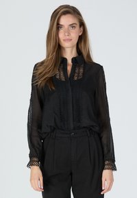 Black sheer blouse with lace detailing, button collar, and long sleeves; features intricate patterns along the front and sleeve edges.