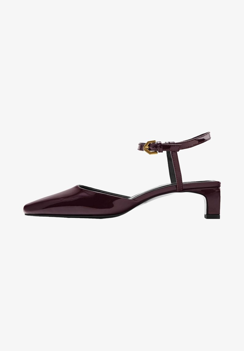 Chaussure femme en cuir verni bordeaux foncé à talon bas, bout pointu et bride cheville avec boucle dorée.
