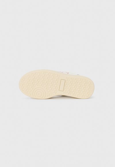 Semelle d'une sneaker en caoutchouc blanc cassé avec un motif en nid d'abeille et un emblème circulaire. Présente une surface plate et texturée pour la traction.
