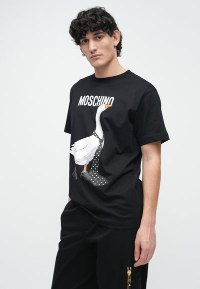 Čierne bavlnené tričko s grafikou bielej husi s bodkovanou kravatou a čiernymi topánkami. Nad grafikou je nápis "Moschino" v bielej farbe.