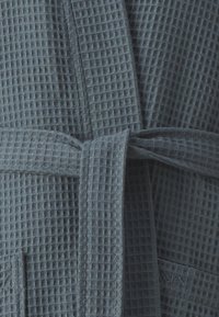 Vaffle-textúrájú, sötétszürke fürdőköntös, amelyhez megkötős öv, széles gallér és steppelt díszítés tartozik, puha anyagból készült a kényelem érdekében.