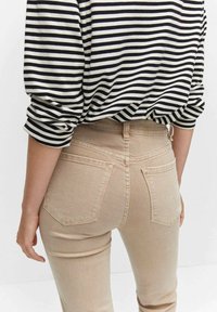Jeans beige de cintura alta con una silueta ajustada, que cuentan con bolsillos traseros y costuras sutiles. La parte superior es de rayas blancas y negras con mangas largas.