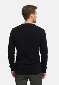 Sort strikkegenser med et strukturert mønster, rund hals og lange ermer. Stoffet ser varmt og lett ut.