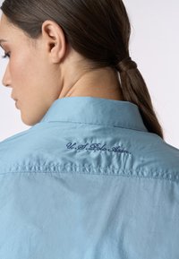 Maglietta azzurra chiara con colletto e dettaglio ricamato "U.S. Polo Assn." sulla schiena, che mette in evidenza una texture di tessuto liscia.