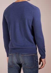 Mörkblå stickad tröja med lång ärm, rundad hals och ribbade mudd och nederkant. Matchas med mörka denimjeans med synlig sömnad.