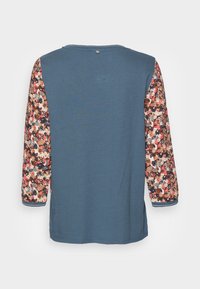 Pitkähihainen T-paita, jossa sininen vartalo ja kukkakuosiset hihat punaisissa, kermankeltaisissa ja ruskeissa sävyissä. Pyöreä pääntie, rento istuvuus.