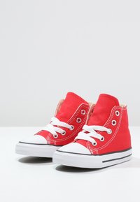 Rote Canvas-Hochschnitt-Sneaker mit weißen Gummisohlen, Schnürsenkeln und Akzenten. Mit Metallösen und einer strukturierten Stoffoberfläche.
